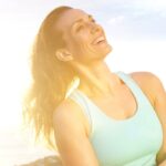 Woman smiling and clasping her arms around herself while hiking on a sunny day