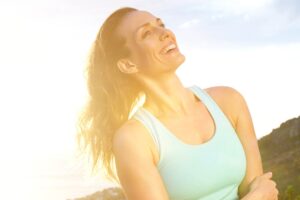 Woman smiling and clasping her arms around herself while hiking on a sunny day